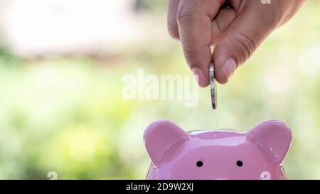 En sauvant, les hommes ont mis des pièces de monnaie dans la banque de cochon y compris le fond vert flou. Banque D'Images
