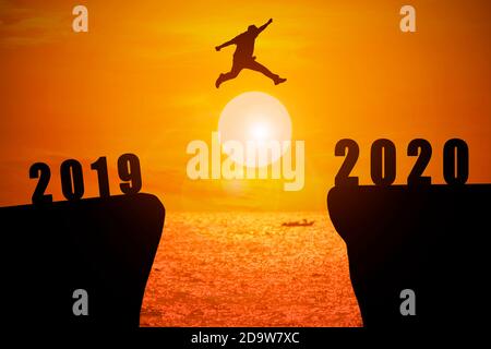 Silhouette de jeunes hommes d'affaires qui sautent de la falaise a le numéro d'année 2019 à côté qui a l'année numéro 2020 avec le soleil se lève à Banque D'Images