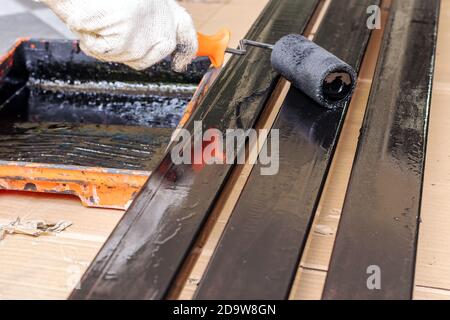 Le peintre porte des gants en tissu, en utilisant un rouleau de peinture noir sur la tige en acier. Banque D'Images