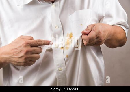 Personne pointant vers une tache de curry renversée sur une chemise blanche. Banque D'Images