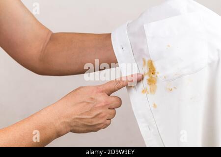 Personne pointant vers une tache de curry renversée sur une chemise blanche. Banque D'Images