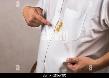 Personne pointant vers une tache de curry renversée sur une chemise blanche. Banque D'Images