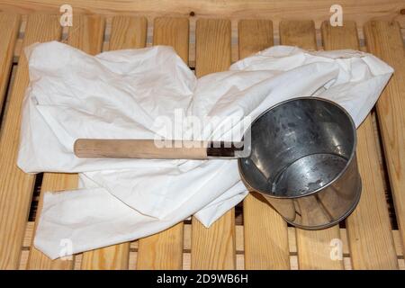 Sauna ou bain, intérieur et accessoires : louche galvanisée avec une longue poignée, une serviette ou une feuille. Banque D'Images