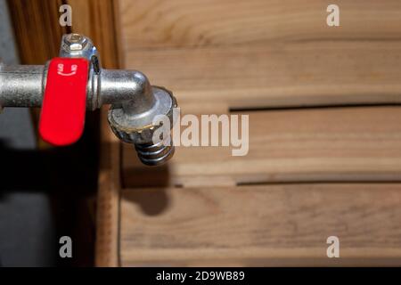 Gros plan d'un robinet simple et rétro pour le recrutement de l'eau avec une poignée rouge dans un sauna chaud, espace de copie, élément de conception. Banque D'Images