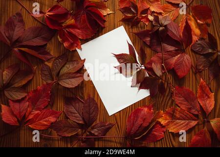 Feuilles d'automne rouges et papier vierge avec espace pour le texte, sur fond en bois. Composition de fond d'automne. Encore la vie des feuilles d'automne. Banque D'Images