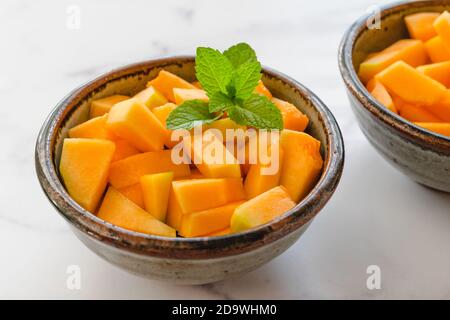 Cubes de melon en forme de cantaloup servis avec des feuilles de menthe en gros plan dans un bol sur fond de marbre clair. Salade de fruits, dessert Banque D'Images