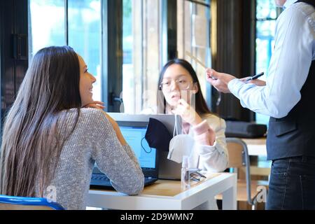 Serveur caucasien prenant la commande de clients dans un restaurant pendant l'épidémie de coronavirus. Nouvelle norme dans les restaurants. Pandémie de coronavirus. Banque D'Images