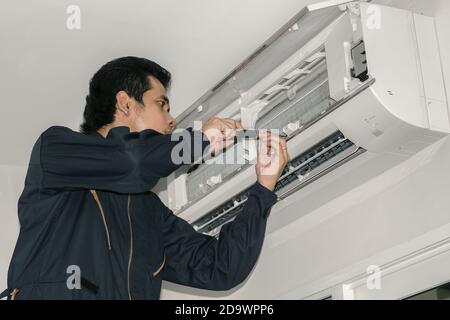 Les réparateurs de climatisation en uniforme bleu vérifient et réparent l'air suspendu au mur. Banque D'Images