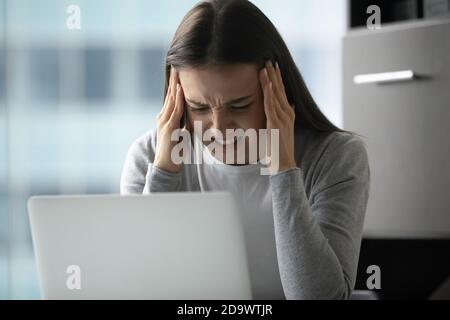 Femme nerveuse employée de bureau qui se serre la tête dans la panique avant l'ordinateur portable