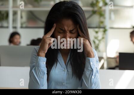 Femme biraciale anxieuse stressée assise avec les yeux fermés frottant les temples Banque D'Images