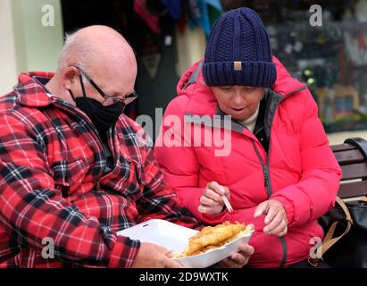 Homme et femme avec plateau de poisson et de frites à manger dans la rue. ROYAUME-UNI. Banque D'Images