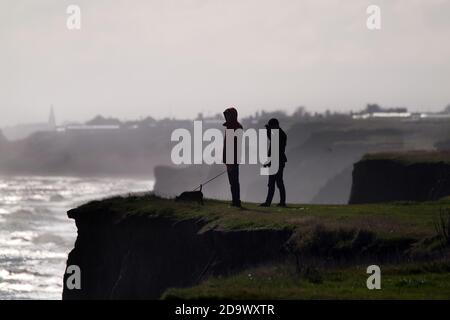 Couple en chien de marche silhouette sur le sommet de la falaise de la côte est. Yorkshire. ROYAUME-UNI. Banque D'Images