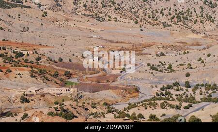 Vue aérienne sur une vallée isolée dans les montagnes Altas près d'Imilchil, au Maroc, avec une route menant à travers et parsemée d'arbres sur les montagnes clairsemées. Banque D'Images