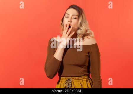 Portrait de la femme blonde endormie et fatiguée dans un chemisier marron bâchant et couvrant la bouche avec le bras, se sentant somnolent après une nuit sans sommeil, manque d'énergie. Indoo Banque D'Images