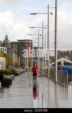 Glasgow, Écosse, Royaume-Uni. Un jogging en chemise rouge court sous la pluie le long de la rivière Clyde dans le centre-ville de Glasgow Banque D'Images