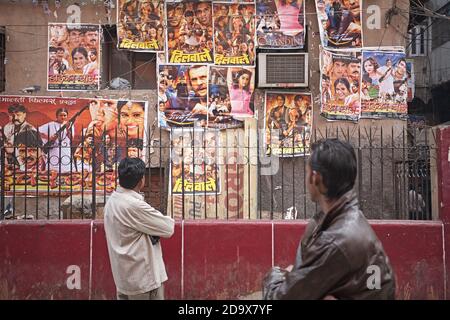 Delhi, Inde, janvier 2008. Deux hommes regardent des affiches de film de Bollywood attachées au mur. Banque D'Images