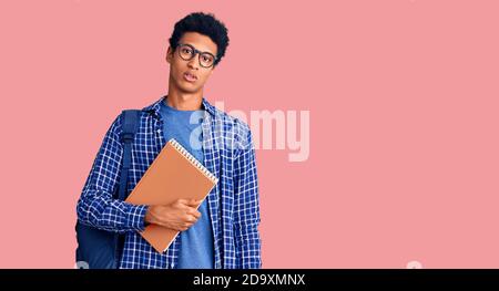 Jeune homme afro-américain portant le sac à dos étudiant tenant le livre qui a l'air endormi et fatigué, épuisé pour la fatigue et la gueule de bois, les yeux paresseux dans la mornin Banque D'Images