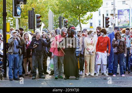 Bristol UK : un groupe de personnes déguisées en zombies et spectateurs attendent pour traverser la route tout en suivant la route de la Bristol Zombie Walk Banque D'Images