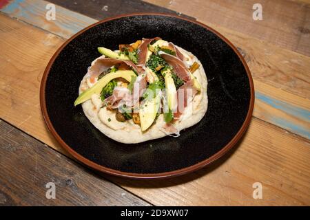 Une délicieuse assiette de pain plat naan avec houmous, champignons, jambon Serrano et avocat sur un plan de travail de cuisine en bois Banque D'Images