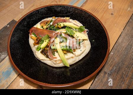 Une délicieuse assiette de pain plat naan avec houmous, champignons, jambon Serrano et avocat sur un plan de travail de cuisine en bois Banque D'Images