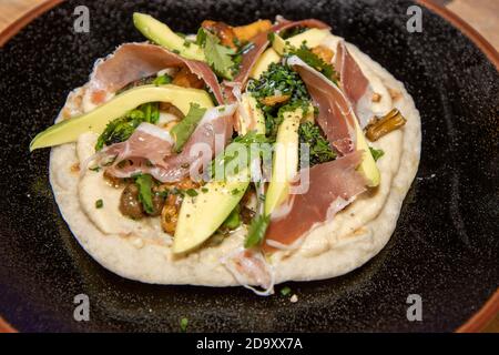 Une délicieuse assiette de pain plat naan avec houmous, champignons, jambon Serrano et avocat sur un plan de travail de cuisine en bois Banque D'Images