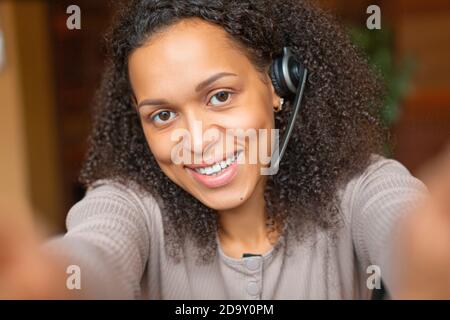 Gros plan une femme afro-américaine avec un casque passe un appel en ligne. Elle regarde la caméra et sourit. Banque D'Images
