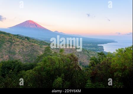 Paysage de la côte nord de Bali au lever du soleil, avec le sommet du volcan du Mont Agung et les pentes forestières, et la mer de Java, depuis le sommet de la colline près d'Amed, Bali, Indonésie Banque D'Images