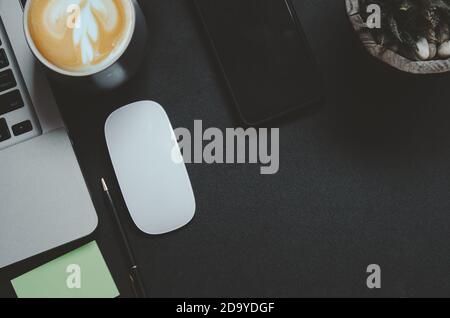 Bureau avec vue sur le dessus ordinateur portable, souris, smartphone, tasse à café et stylo sur table noire. Banque D'Images