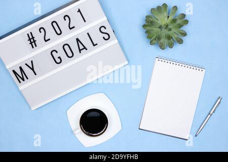 Bureau - vue de dessus. Carnet, stylo, tasse à café, succulent, visionneuse avec texte My Goals 2021 sur un bureau bleu. Plans pour le concept de l'année à venir Banque D'Images