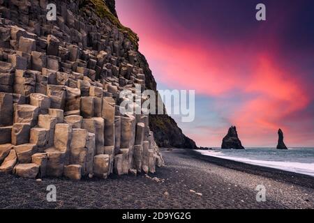 Vue incroyable sur Black Beach et les falaises de Troll toes au coucher du soleil. Grand ciel violet brillant sur fond. Reynisdrangar, Vik, Islande. Photographie de paysage Banque D'Images