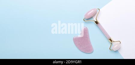 Bannière horizontale mode avec masseur Gua Sha et Rose Quartz rouleau de jade sur fond bleu - image Banque D'Images