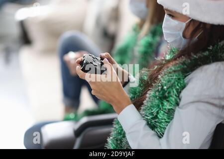 Deux amies sont assises sur le canapé avec des manettes de jeu dans les chapeaux du père noël et les masques médicaux de protection Banque D'Images