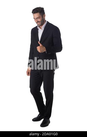 Portrait complet d'un jeune homme d'affaires beau en noir costume souriant et de montrer le pouce vers le haut studio isolé sur blanc arrière-plan Banque D'Images