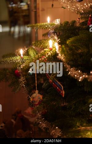 Gros plan d'une branche d'arbre de Noël avec bougies allumées, couronne, boules colorées scintillantes à l'intérieur le soir. Vert classique, rouge couleur de Noël Banque D'Images