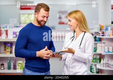 le pharmacien amical caucasien a une belle conversation avec un client, aide à trouver un médicament, pose des questions sur les symptômes et de ce qui est il souffre Banque D'Images