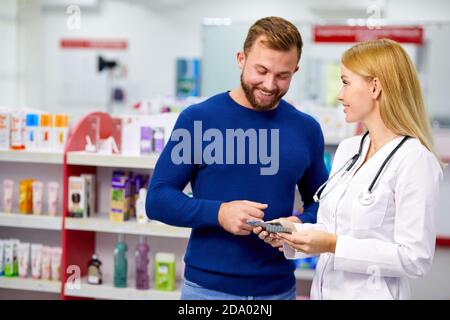 le pharmacien amical caucasien a une belle conversation avec un client, aide à trouver un médicament, pose des questions sur les symptômes et de ce qui est il souffre Banque D'Images