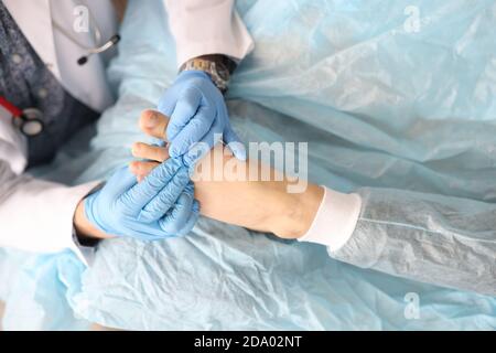 Dermatologue tient le pied de la femme avec le pouce endommagé dedans ses mains dans des gants en caoutchouc en clinique Banque D'Images