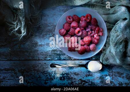 Framboises fraîches en bol et cuillère avec sucre sur bois Table et tissu argenté Banque D'Images