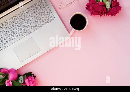 Ordinateur portable, pivoines et café sur tabl rose Banque D'Images