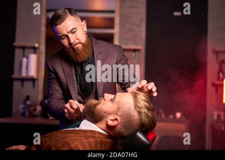 client de l'hippopotame caucasien visite au salon de coiffure rasage de la barbe par coiffeur professionnel, barbe élégante et moderne en salon Banque D'Images