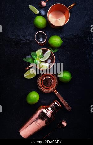 Préparation du cocktail Mule de Moscou avec de la bière au gingembre, de la vodka, du citron vert et de la glace. Outils à barre en cuivre. Arrière-plan du compteur de barres noires. Vue de dessus. Copier l'espace Banque D'Images