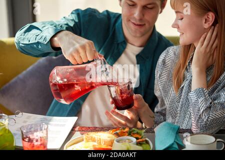 un jeune homme galant verse des jus de boisson sucrée dans des verres pour femmes, les traite. au café, au restaurant Banque D'Images