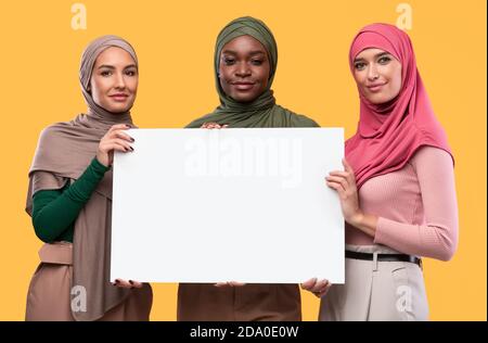 Trois musulmanes tiennent un tableau vierge pour le texte, fond jaune Banque D'Images