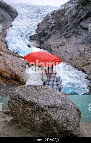 Glacier Briksdal (Briksdalbreen), Norvège. Couple avec un parapluie assis sur un rocher qui regarde le glacier Briskdal. Vue sur le glacier il y a 10 ans. Banque D'Images