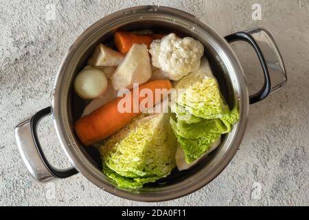 Carottes, racines de céleri, oignons et autres ingrédients pour préparer un bouillon de légumes ou une soupe dans une casserole Banque D'Images