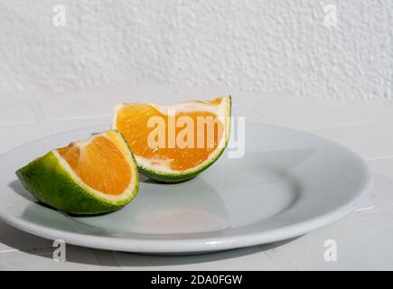 Tangerine verte coupée en morceaux sur une plaque blanche. Banque D'Images