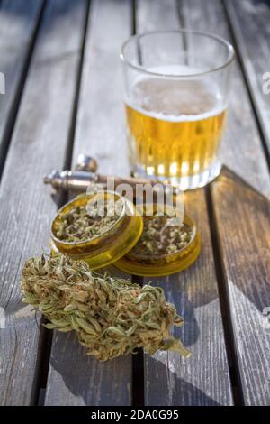 Table avec broyeur de marijuana, bouton de marijuana, un tube de fumée et un verre de bière en arrière-plan. Banque D'Images