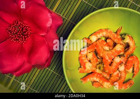 Crevettes dans un bol vert profond sur le tapis de bambou avec fleur rouge. Crevettes frites de style asiatique. Banque D'Images