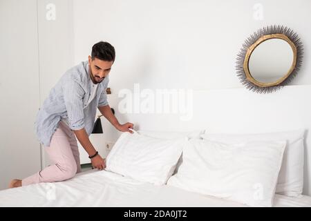 Homme calme portant des vêtements domestiques faisant un lit doux dans confortable chambre après réveil le matin Banque D'Images