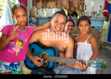 Intérieur d'une maison traditionnelle à Rangiroa, îles Tuamotus, Polynésie française, Pacifique Sud. Homme jouant de la guitare et singuin avec sa famille. Banque D'Images